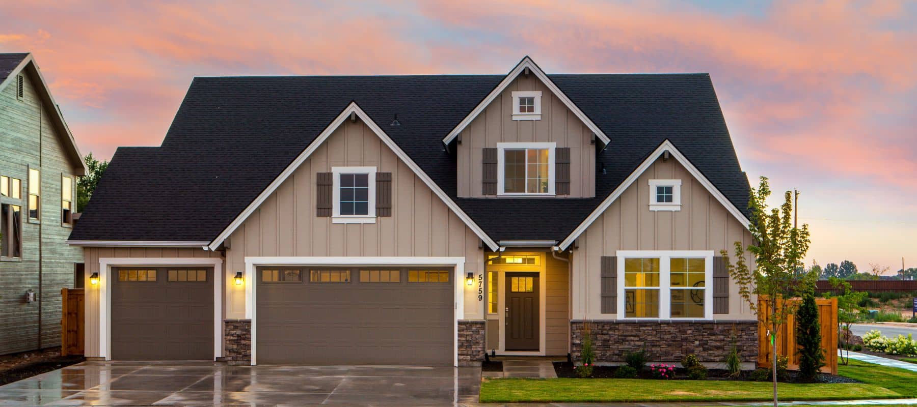 Modern suburban home with fresh beige siding, dark roof, and stone accents under a colorful evening sky