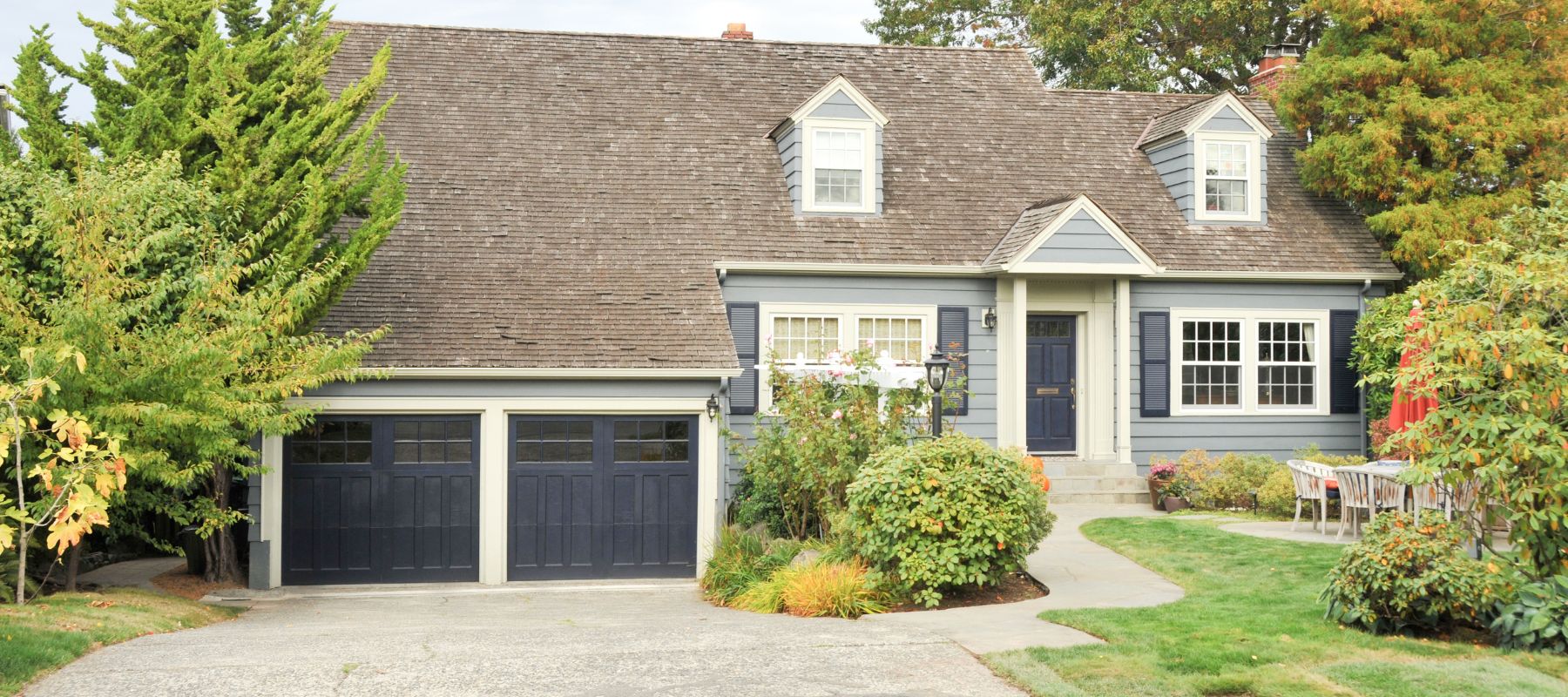 Blue-gray house with a wooden shingle roof and lush landscaping in front
