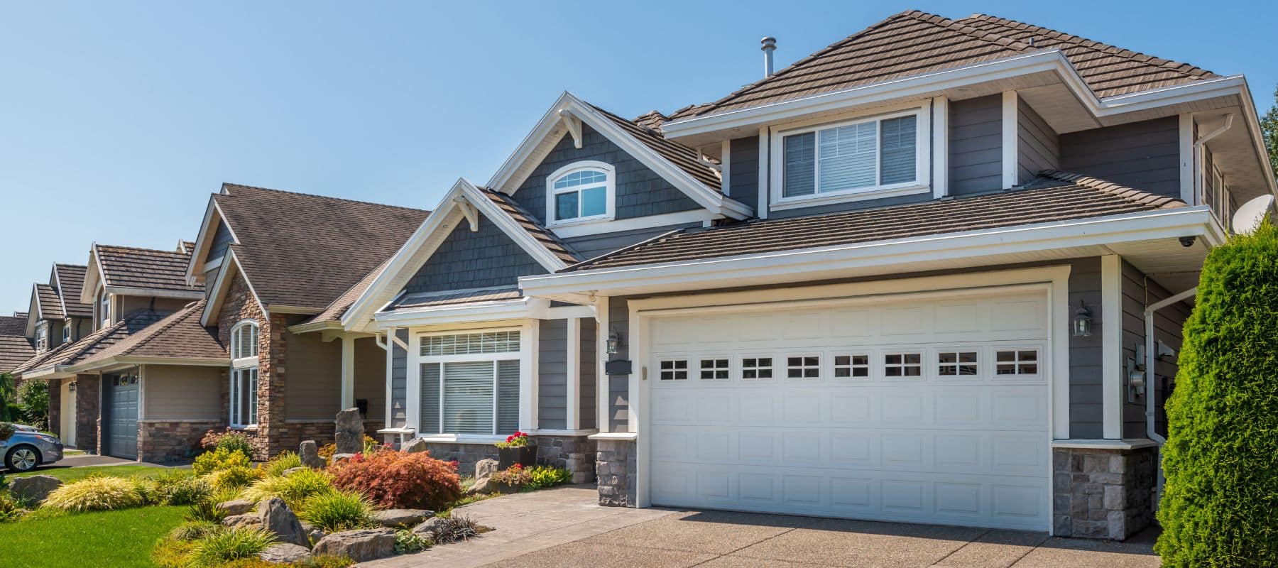 Modern suburban home with gray siding, white trim, and a landscaped front yard under clear blue skies
